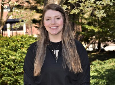 Sarah Hall smiling at the camera and standing in front of dogwood trees at the Graduate School