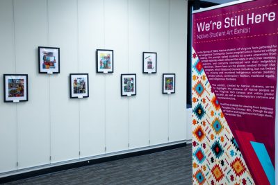 Collages created by Native students at Virginia Tech hang from wires against a white wall.