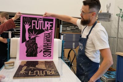 A man holds up a poster with the words “THE FUTURE YOUR HANDS” and a drawing of the Statue of Liberty.