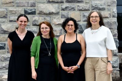 Four women pose for group photo in front of Hokie stone building.