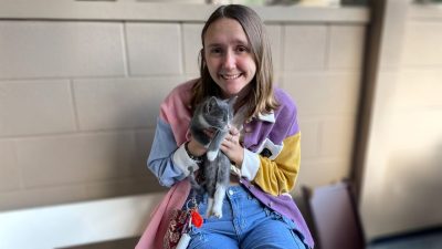 A young woman with long brown hair holds a gray and white kitten.