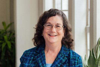 Rachel Holloway, in a turquoise jacket, smiles at the camera