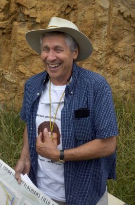 Laughing man wearing hat and holding map stands in front of rock formation.
