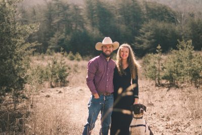 Carmen McBride (at right) standing in a field next to a man and holding a German Shorthaired Pointer