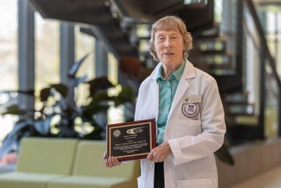 Dr. Marion Ehrich (at center) posing with a plaque in a white lab coat