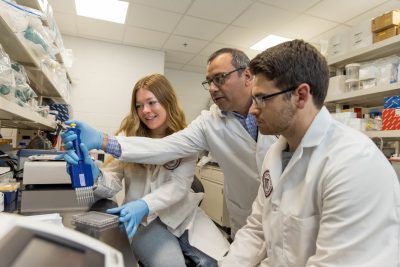 Roger Ramirez-Barrios (at center) holding a pipette assisting students (at right and left) with their laboratory work