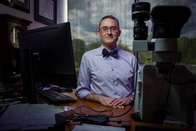Tom Cecere standing in his office between a computer and a microscope.
