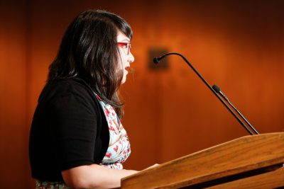 A determined Janine Joseph speaks at a lectern. 