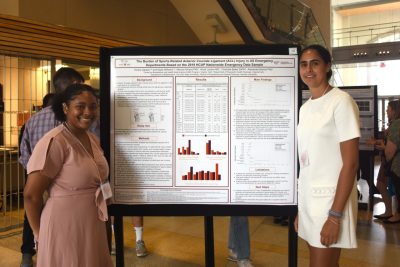 Two students stand next to their research presentation poster.