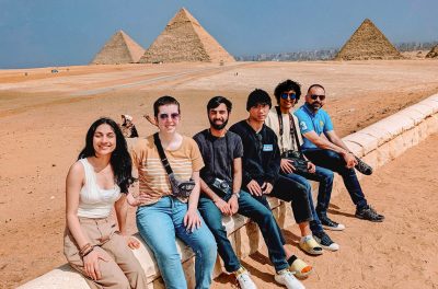 Five students and their professor sitting in front of three pyramids